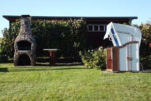Ein Backofen aus Stein, ein Korbstuhl und ein kleiner Tisch in einem Garten.