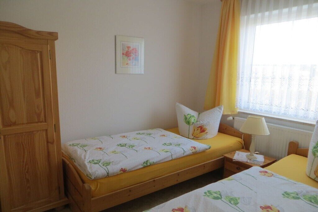 A bedroom with two single beds, a wooden wardrobe, a bedside table with a lamp, and a window with curtains.