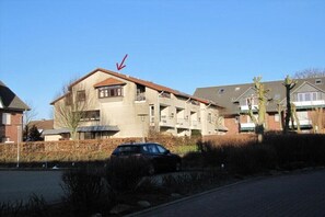 A multi-story residential building with a parking area in front. - Holiday apartment with 1 bedroom (Büsumer Deichhausen)