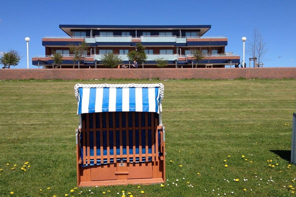 Een strandstoel met een streepjeshoes in een grasveld, met een gebouw op de achtergrond.