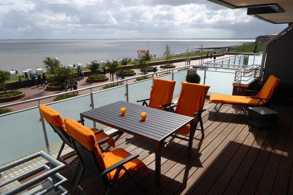 A balcony with a table and chairs, overlooking a body of water and a promenade. - Holiday apartment with 2 bedrooms (Wilhelmshaven)