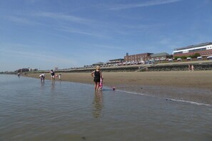 A beach with people walking along the shore, a building in the background, and a clear sky. - Holiday apartment with 2 bedrooms (Wilhelmshaven)