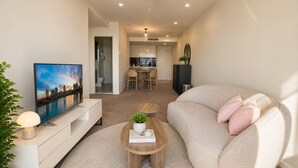 En moderne stue med sofa, sofabord, fjernsyn og et spiseområde i baggrunden.