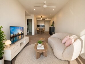A modern living room with a sofa, a coffee table, a TV, and a dining area in the background. - Metropolitan Luxe | Balcony with Skyline Views (Brisbane City)