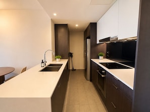 A modern kitchen with a central island, built-in appliances, and a dining area with a table and chairs. - Metropolitan Luxe | Balcony with Skyline Views (Brisbane City)