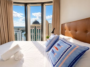 A hotel room with a large bed, a view of a cityscape, and a window with curtains. - Metropolitan Luxe | Balcony with Skyline Views (Brisbane City)