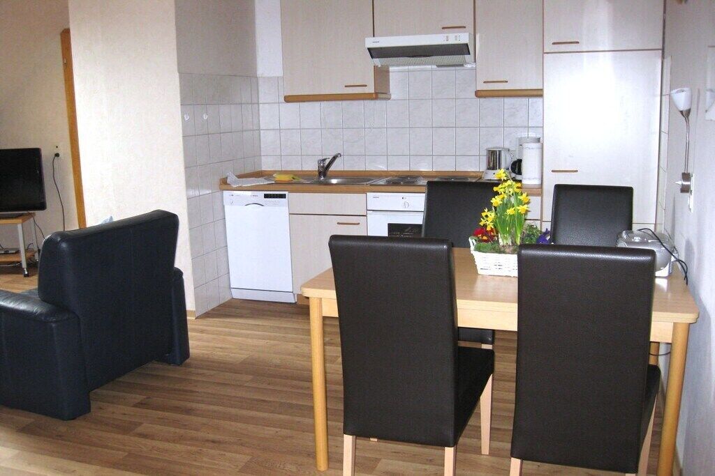 Eine moderne Küche mit weißen Schränken, einer Holz Arbeitsplatte und einem eingebauten Geschirrspüler. Es gibt einen Esstisch mit vier Stühlen und eine Vase mit Blumen.