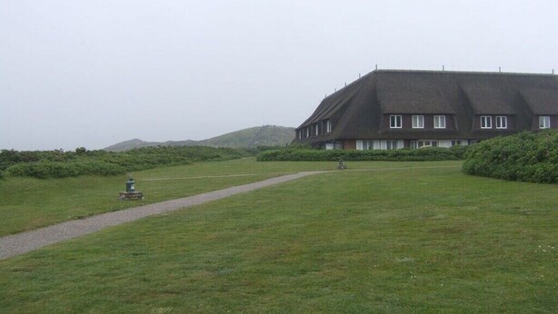 Ein großes Gebäude mit einem steilen Dach, umgeben von einer Wiese und einem Weg, der darauf führt.