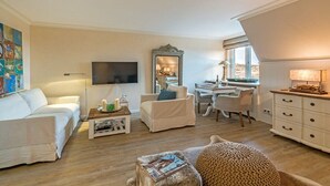 Ein helles Wohnzimmer mit einer Couch, einem Couchtisch und einem Fernseher. Es gibt einen Essbereich mit Tisch und Stühlen.