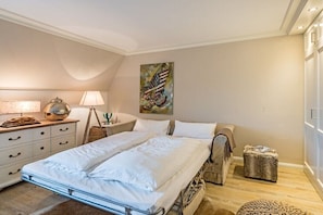 Un dormitorio con cama, mesitas de noche, lámpara, un cuadro y una ventana.