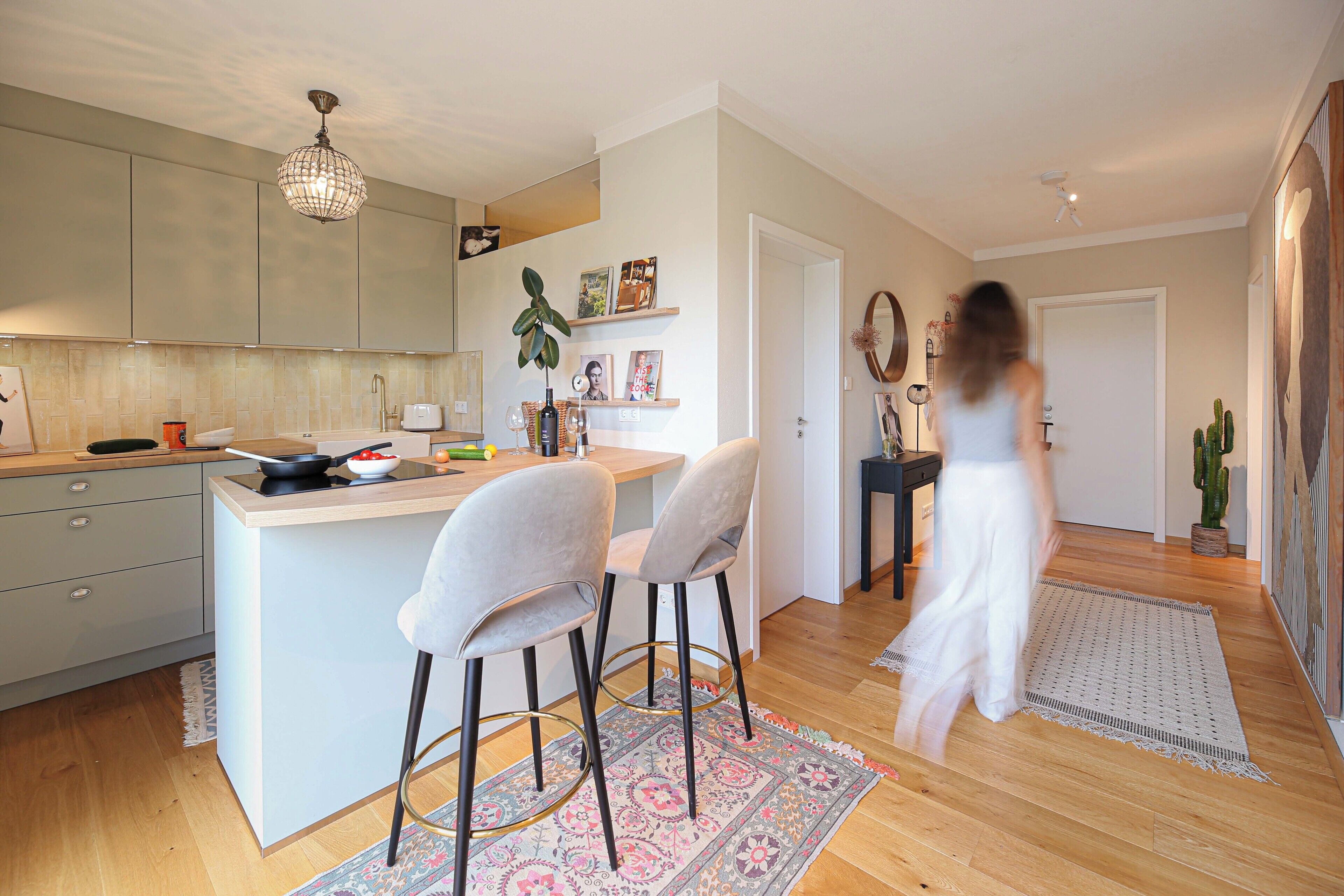 A modern kitchen with a central island, bar stools, and a dining area with a patterned rug.