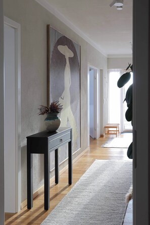 A hallway with a large abstract painting, a console table with a vase, and a rug leading to a door. - Stylish Apartment in the Altmühl Valley (Schernfeld)