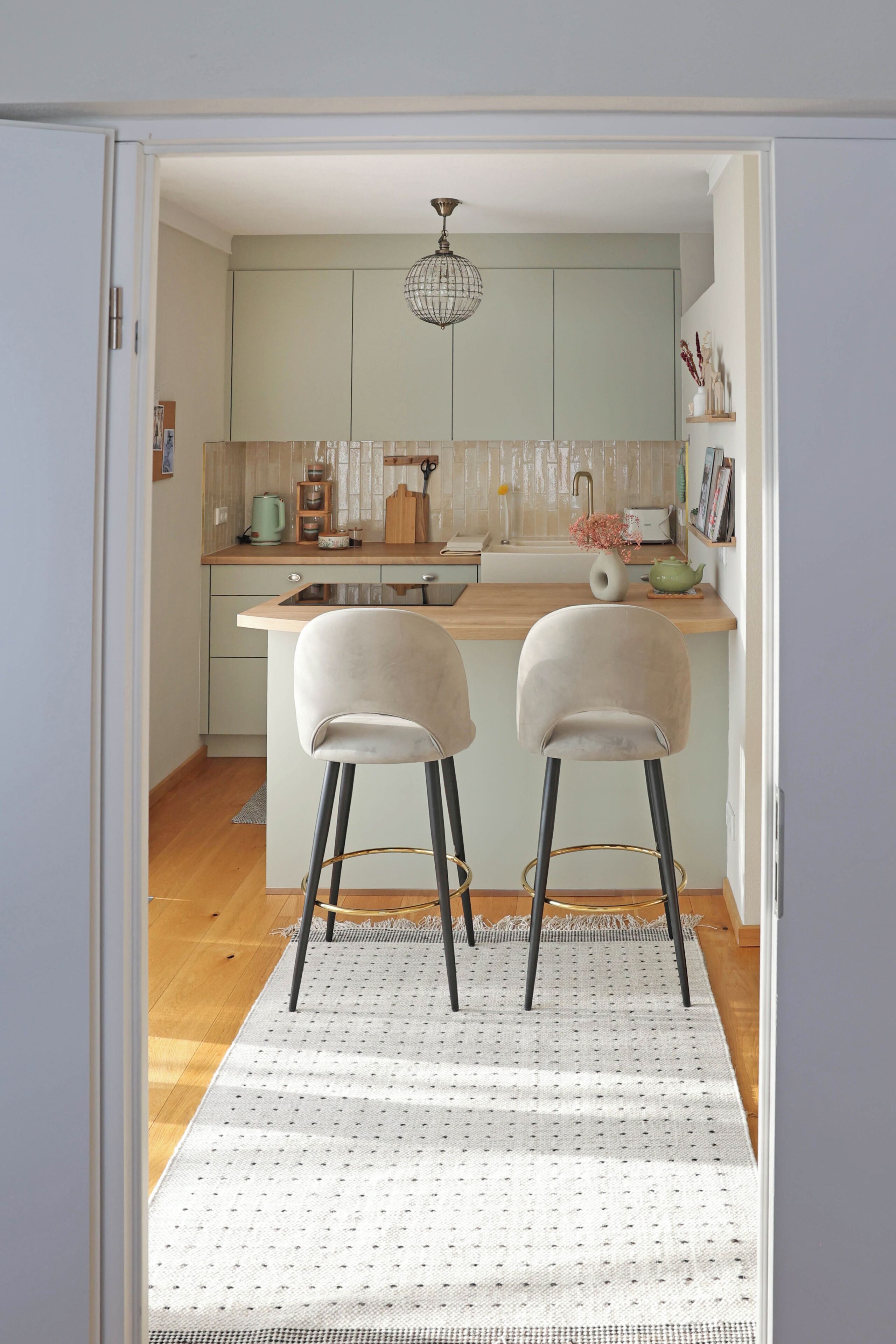 A kitchen with two bar stools, a wooden countertop, and a hanging light fixture.