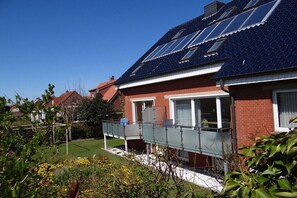 A residential house with a red brick exterior, a balcony with a glass railing, and solar panels on the roof. - Seestern 10 Apartment House Seestern (Norderney)