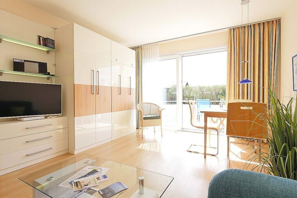 Uma sala de estar moderna com uma mesa de centro de vidro, uma televisão de tela plana e um espaço de refeições com mesa e cadeiras.