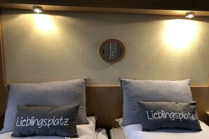 Ein Hotelzimmer mit zwei Betten, jedes mit einem Kopfkissen mit der Aufschrift 'Lieblingsplatz'.