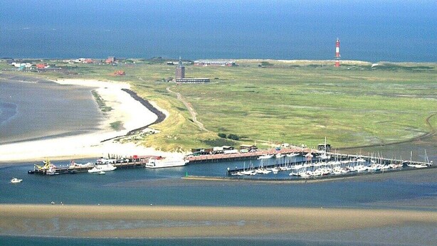 Eine Vogelperspektive einer Küstenlandschaft mit einem Hafen, Booten, einem Leuchtturm und einer kleinen Siedlung.