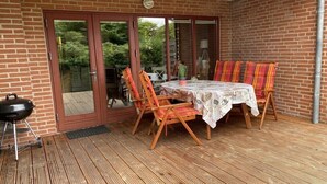 An outdoor patio with a table and chairs, a barbecue grill, and a sliding glass door leading to a garden. - Holiday apartment in Holnis with Wi-Fi (Holnis)