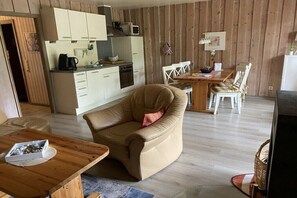 Una sala de estar acogedora con un sillón de cuero, una mesa de comedor de madera y una zona de cocina con armarios blancos y un microondas.
