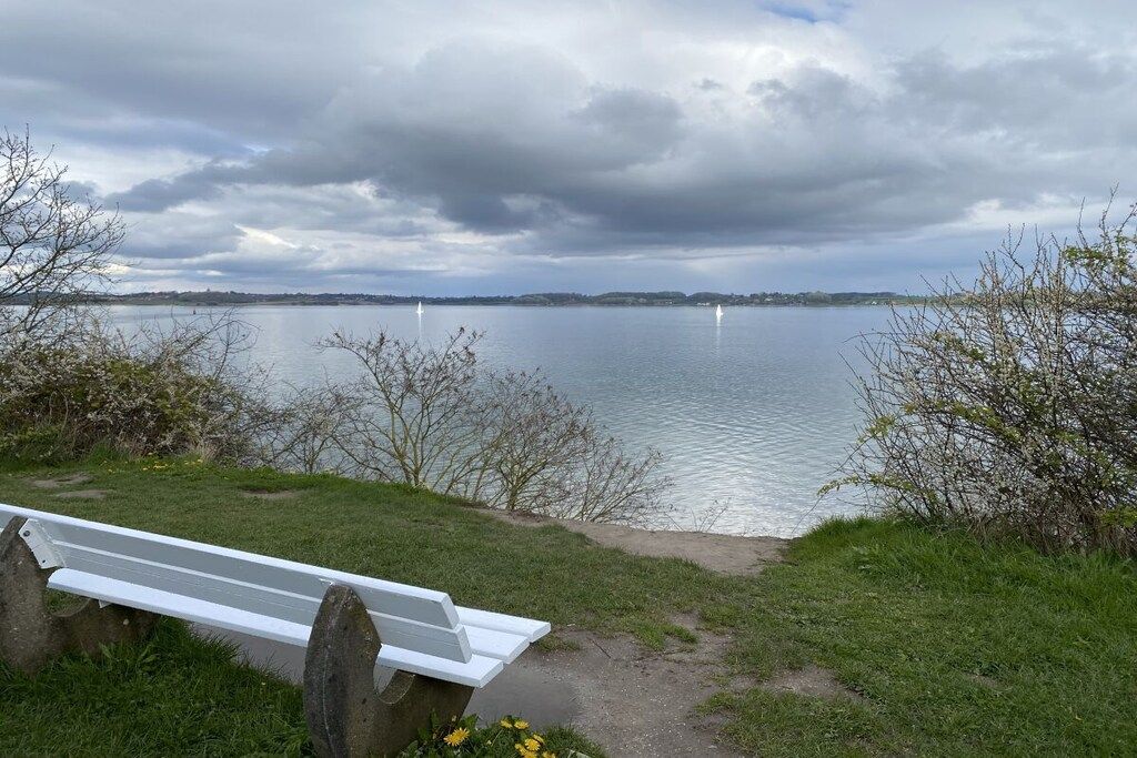 A bench overlooking a lake with a cloudy sky.