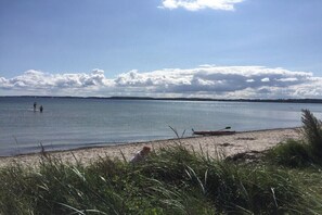 Una playa con agua tranquila, un bote en la orilla y gente en el agua.