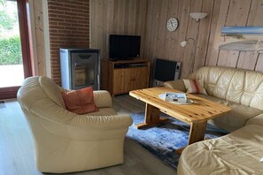 Una sala de estar con una mesa de centro de madera, sofás color beige, un televisor y un reloj en la pared.