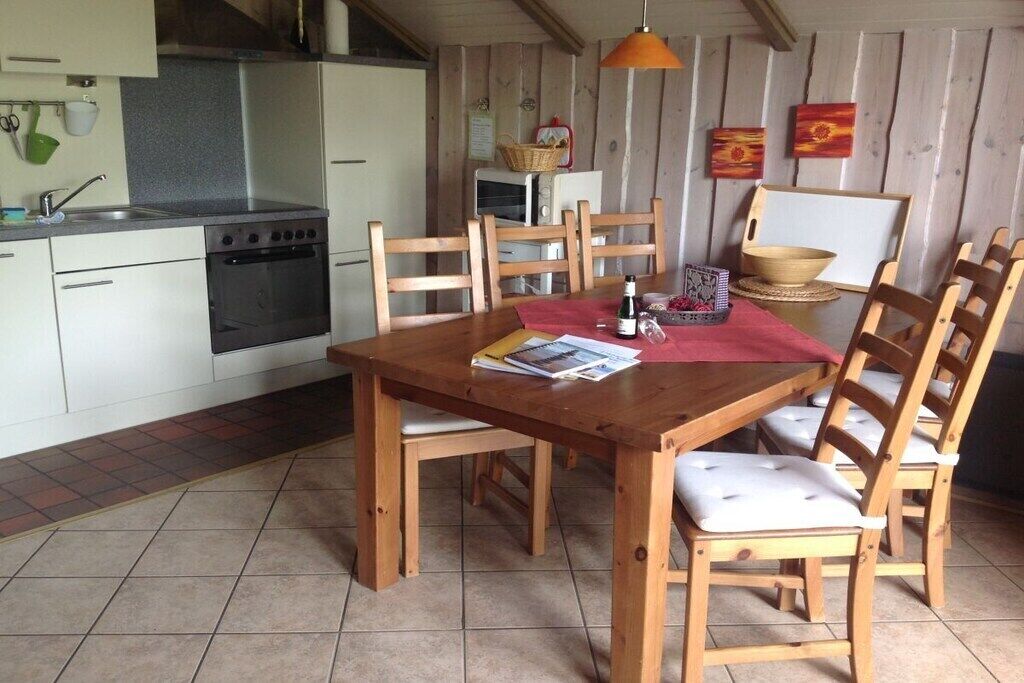 Una cocina con estufa, lavamanos y sillas de madera alrededor de una mesa con un mantel individual rojo.