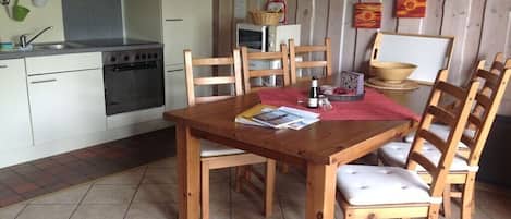 Una cocina con estufa, lavamanos y sillas de madera alrededor de una mesa con un mantel individual rojo.