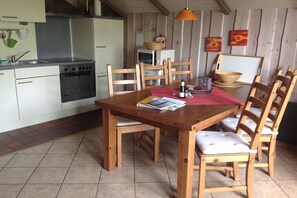 A kitchen with a stove, sink, and wooden chairs around a table with a red placemat. - Holiday apartment in Holnis with Wi-Fi (Holnis)