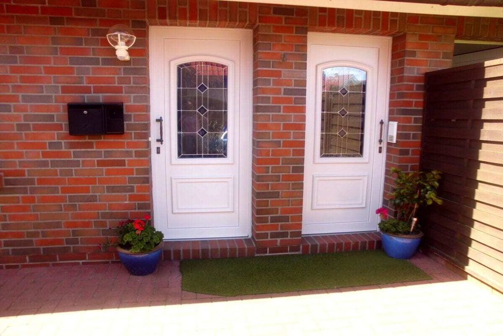 A brick house with two white doors, a mailbox, and potted plants.