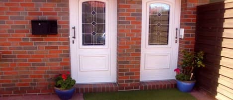 A brick house with two white doors, a mailbox, and potted plants.