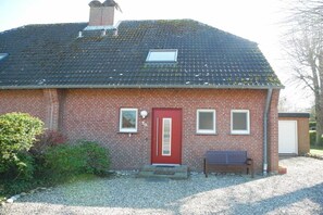 Ein Ziegelhaus mit roter Tür, einem kleinen Fenster und einer Bank davor.