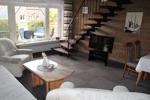 A living room with a sofa, a coffee table, a TV, and a staircase. - Sailor House Semi-detached (Dornumersiel)