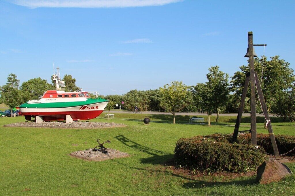 Un bateau est exposé dans un espace verdoyant, avec des arbres et un mât de drapeau en arrière-plan.