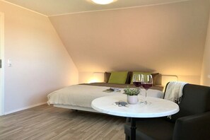 Ein Schlafzimmer mit einem Bett, einem runden Tisch mit Pflanze und Weinglas sowie einem schwarzen Sessel.
