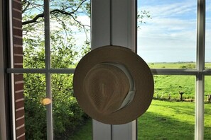 A woven basket hanging on a window with a view of a green field and trees. - Holiday apartment with 1 bedroom (Neuharlingersiel)