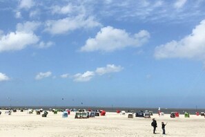 A beach with numerous numbered containers, a clear sky, and a distant view of the sea. - Holiday apartment with 1 bedroom (Neuharlingersiel)