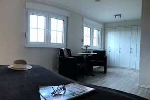 A room with a bed, two windows, a small table with a vase, and a wardrobe. - Holiday apartment with 1 bedroom (Neuharlingersiel)