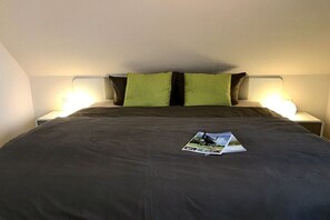 A bed with a dark bedspread, two green pillows, and a magazine on the bed. - Holiday apartment with 1 bedroom (Neuharlingersiel)