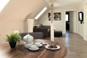 A modern living room with a dining area, featuring a sofa, a table with tea set, and a potted plant. - Holiday apartment with 1 bedroom (Neuharlingersiel)