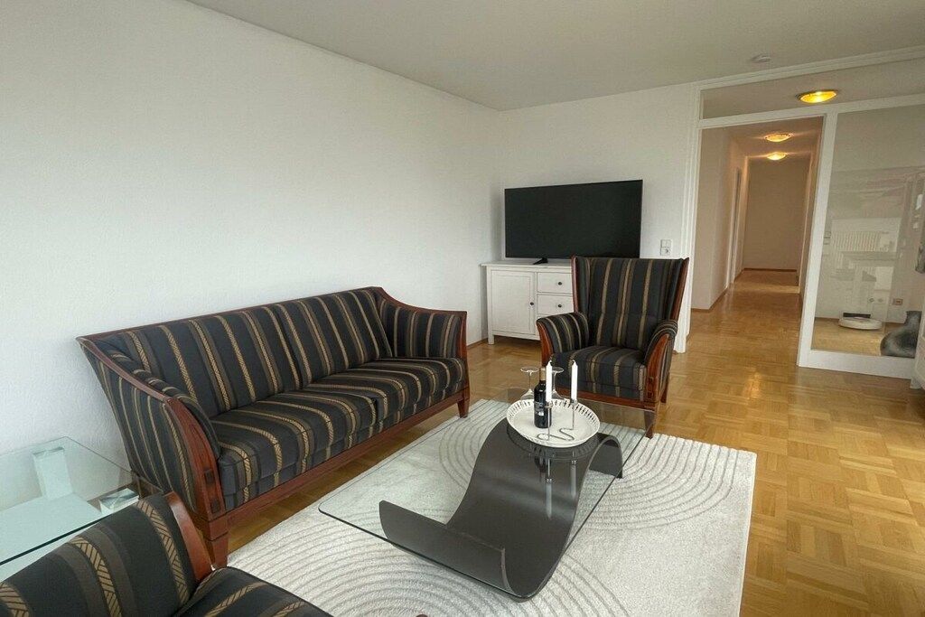 Ein Wohnzimmer mit einer Couch, Sesseln, einem Couchtisch und einem Flachbildfernseher.