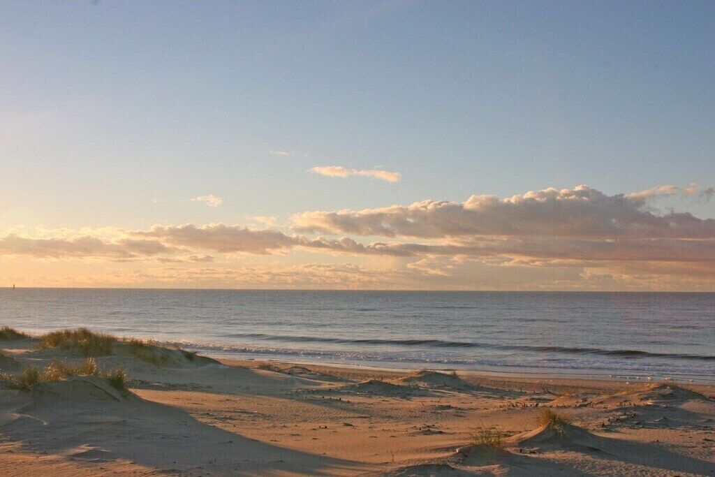 Une plage avec des dunes de sable et une mer calme sous un ciel partiellement nuageux.