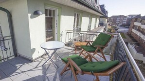 A balcony with a table and two chairs, a window, and a view of the surrounding buildings. - Holiday apartment in Sylt with swimming pool (Sylt)