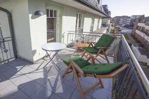 Een balkon met een tafel, twee stoelen, een raam en uitzicht op de omliggende gebouwen.