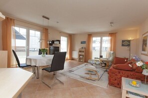 A well-lit living room with a dining area, a sofa, and a TV. - Holiday apartment in Sylt with swimming pool (Sylt)
