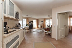 A spacious kitchen with modern appliances, a dining area with a table and chairs, and a view of the outdoors through large windows. - Holiday apartment in Sylt with swimming pool (Sylt)
