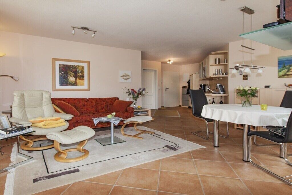Ein Wohnzimmer mit einer Couch, einem Esstisch mit Stühlen und einer Küche im Hintergrund.