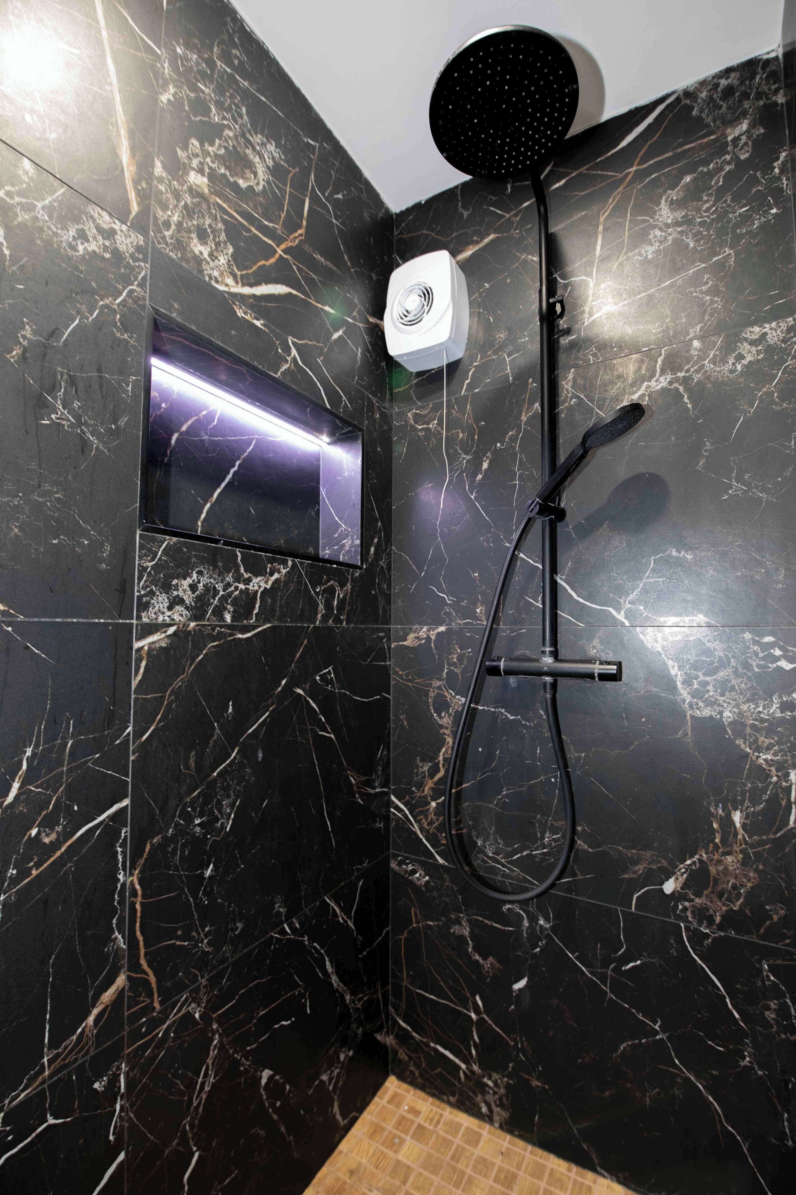 Ein modernes Badezimmer mit schwarzer Marmorwand, einer Handbrause, einem Duschschlauch und einer integrierten LED-Leuchtafel.