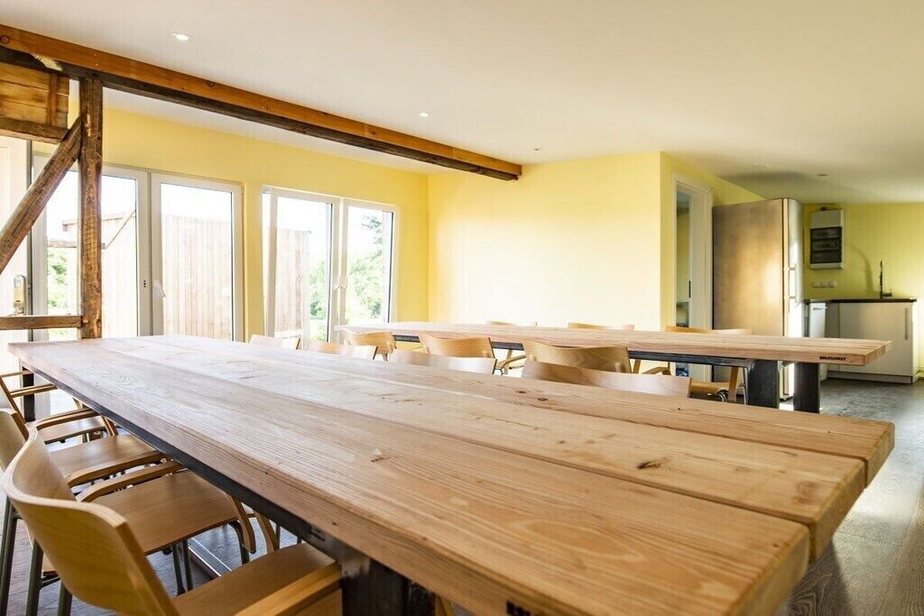 Una habitación amplia con una larga mesa de madera y sillas, una escalera y una zona de cocina.