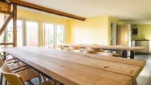 A spacious room with a long wooden table and chairs, a staircase, and a kitchen area. - Holiday apartment with 1 bedroom (Schwedeneck)